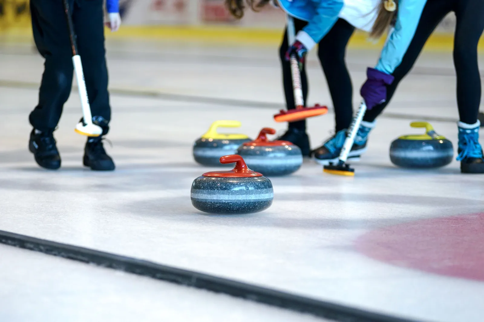 Curlingpelaajat harjaavat kiven edestä jäällä