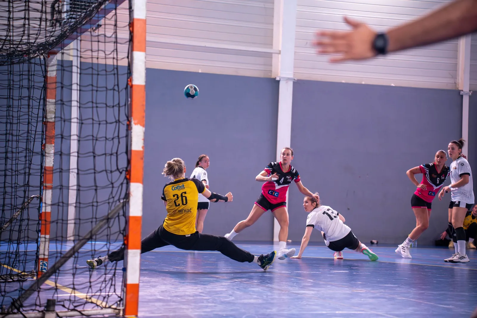 Käsipalloilija laukoo maalia kohti, maalivahti torjuu