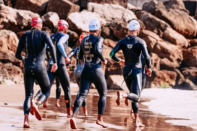 Triathlonistit märkäpuvuissa juoksevat uintiosuudelle